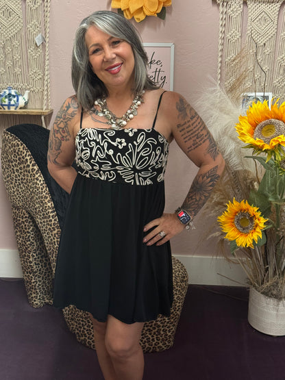 Woman in a black dress with white patterns standing in a room with decorative elements.