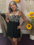 Woman in a black dress with white patterns standing in a room with decorative elements.